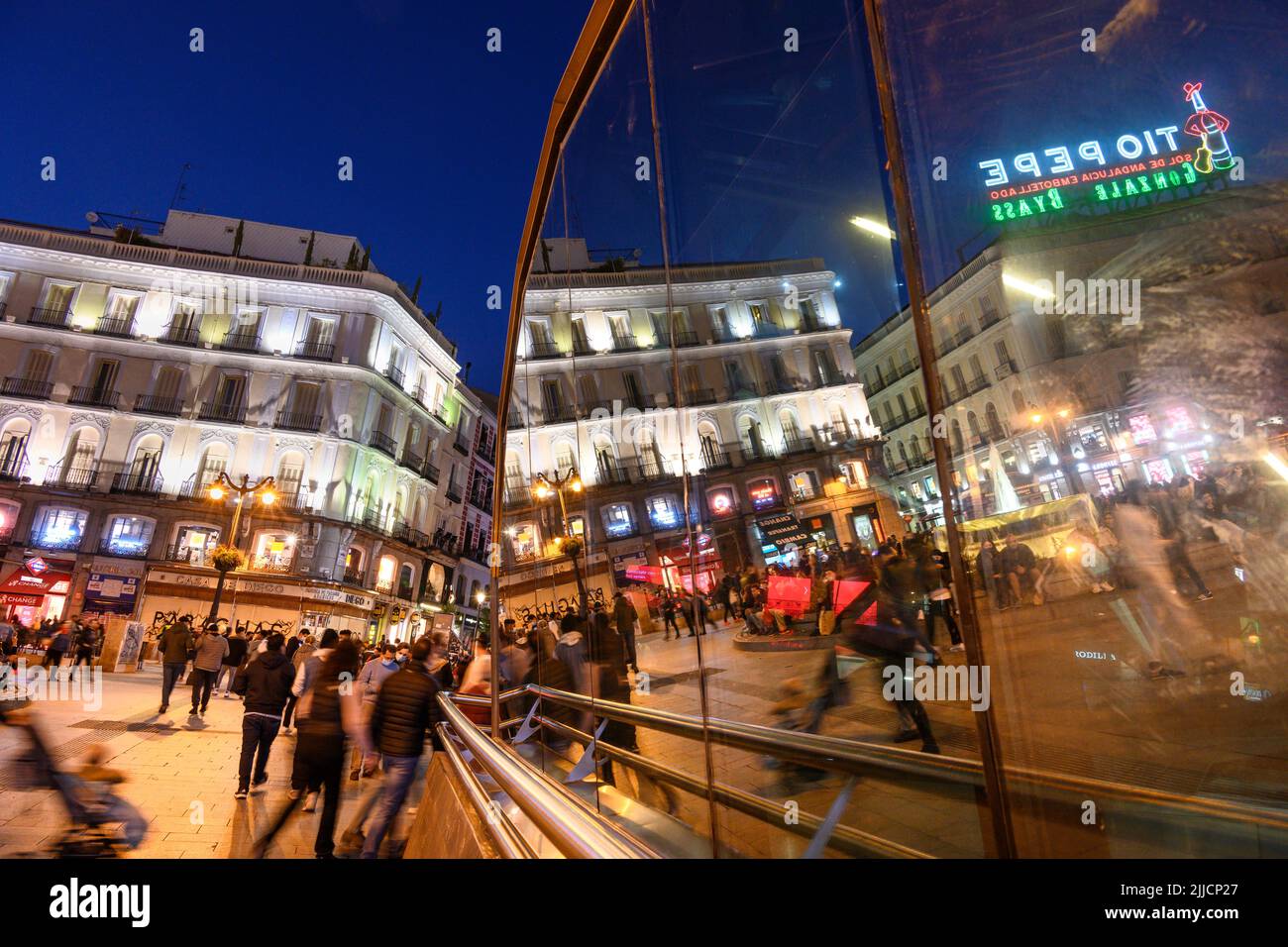 Crowds in The Puerta del Sol, at night with the famous Tio Pepe advertising sign reflected in the windows of the Sol Metro station.  Madrid, Spain. Stock Photo