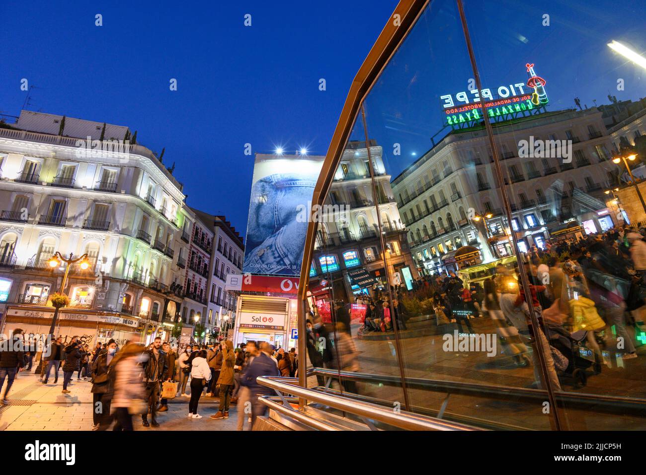 Crowds in The Puerta del Sol, at night with the famous Tio Pepe advertising sign reflected in the windows of the Sol Metro station.  Madrid, Spain. Stock Photo