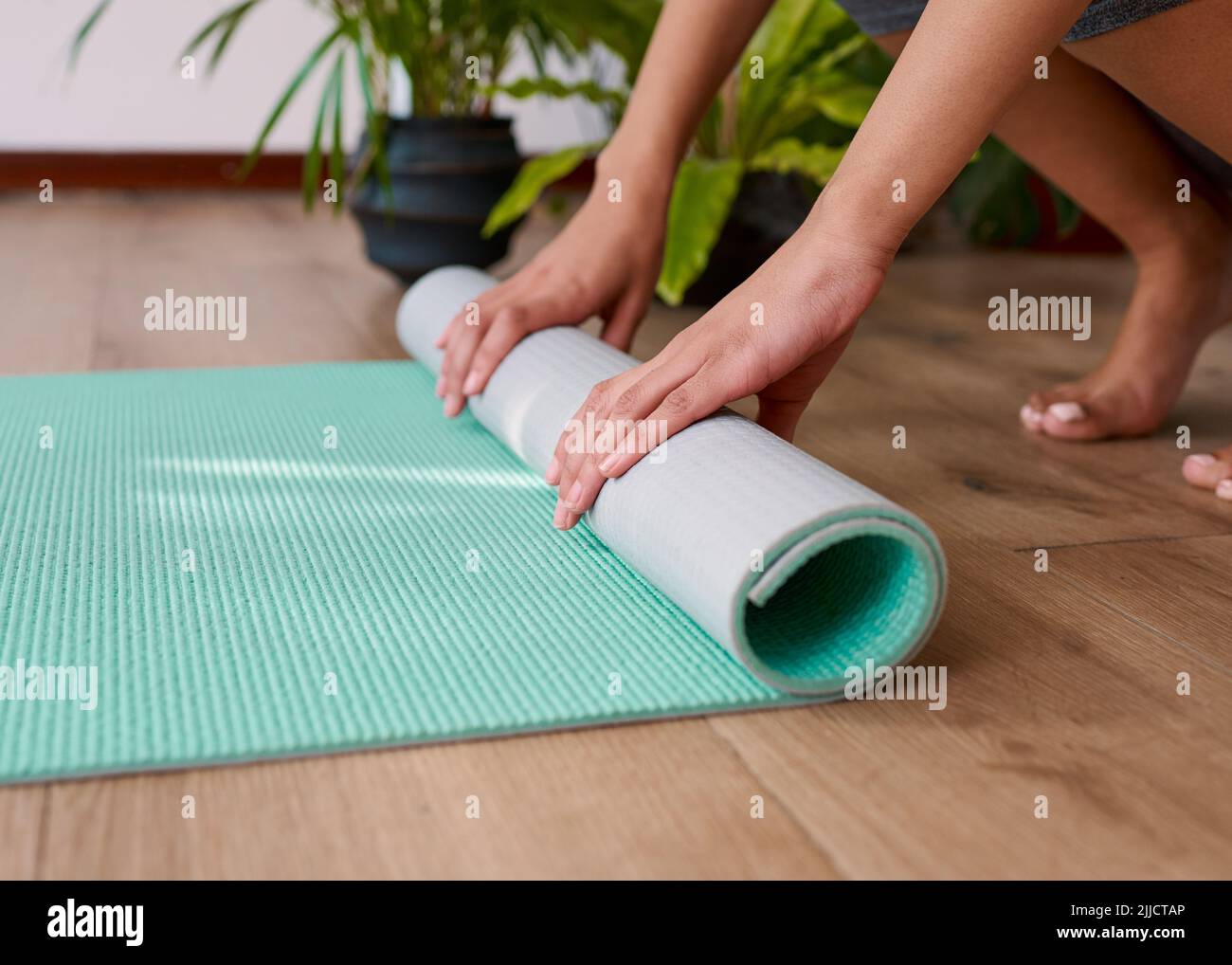 A young multiethnic woman rolls up her yoga mat at the end of her
