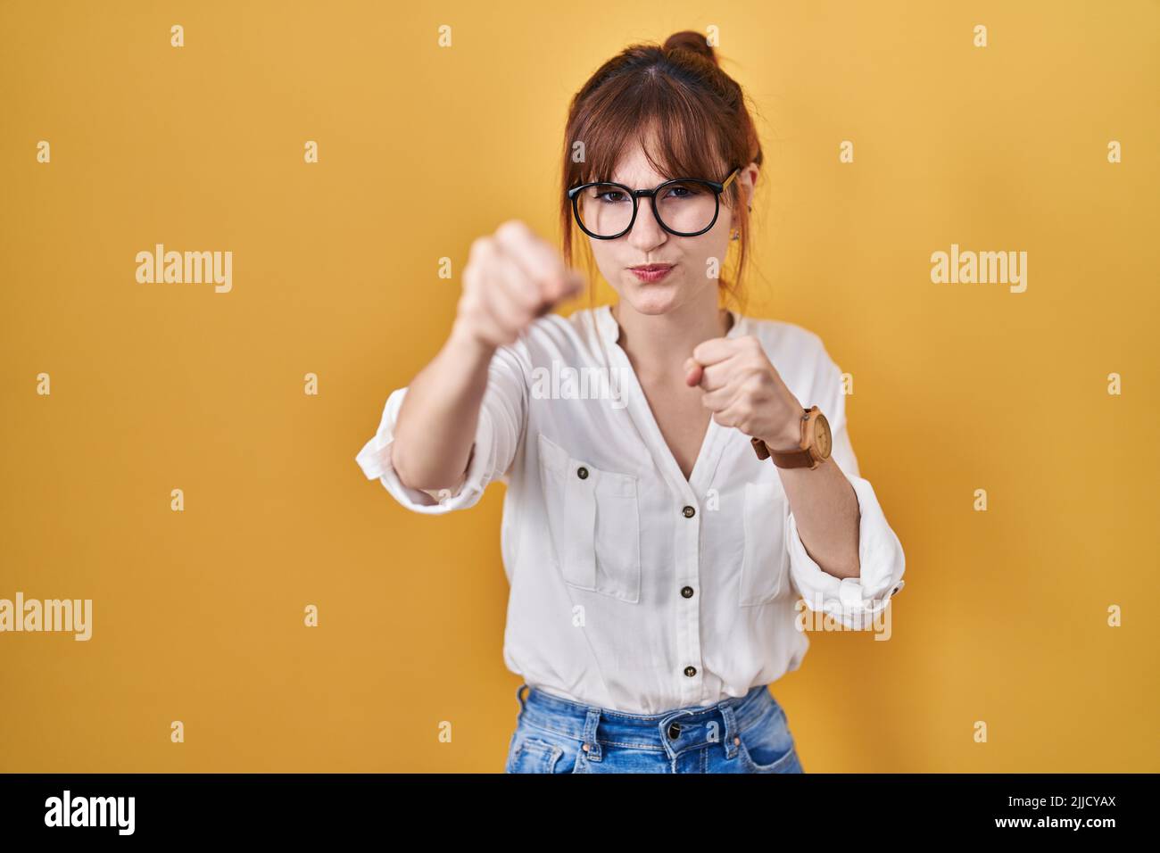 Young beautiful woman wearing casual shirt over yellow background punching fist to fight, aggressive and angry attack, threat and violence Stock Photo