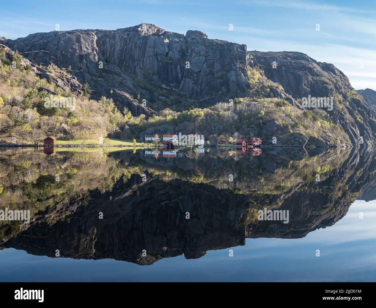 Near Ana-Sira at the norwegian southern coast, lonely houses at feet of a rock formation are reflected in the calm sea, Norway Stock Photo