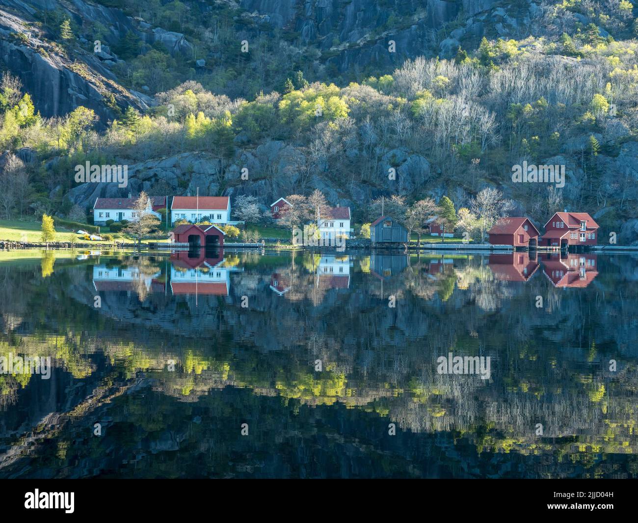 Near Ana-Sira at the norwegian southern coast, lonely houses at feet of a rock formation are reflected in the calm sea, Norway Stock Photo