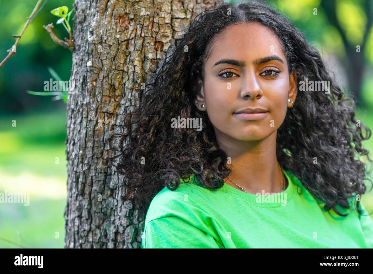 Outdoor portrait of beautiful happy mixed race African American girl teenager female young woman with a natural green leaves background Stock Photo