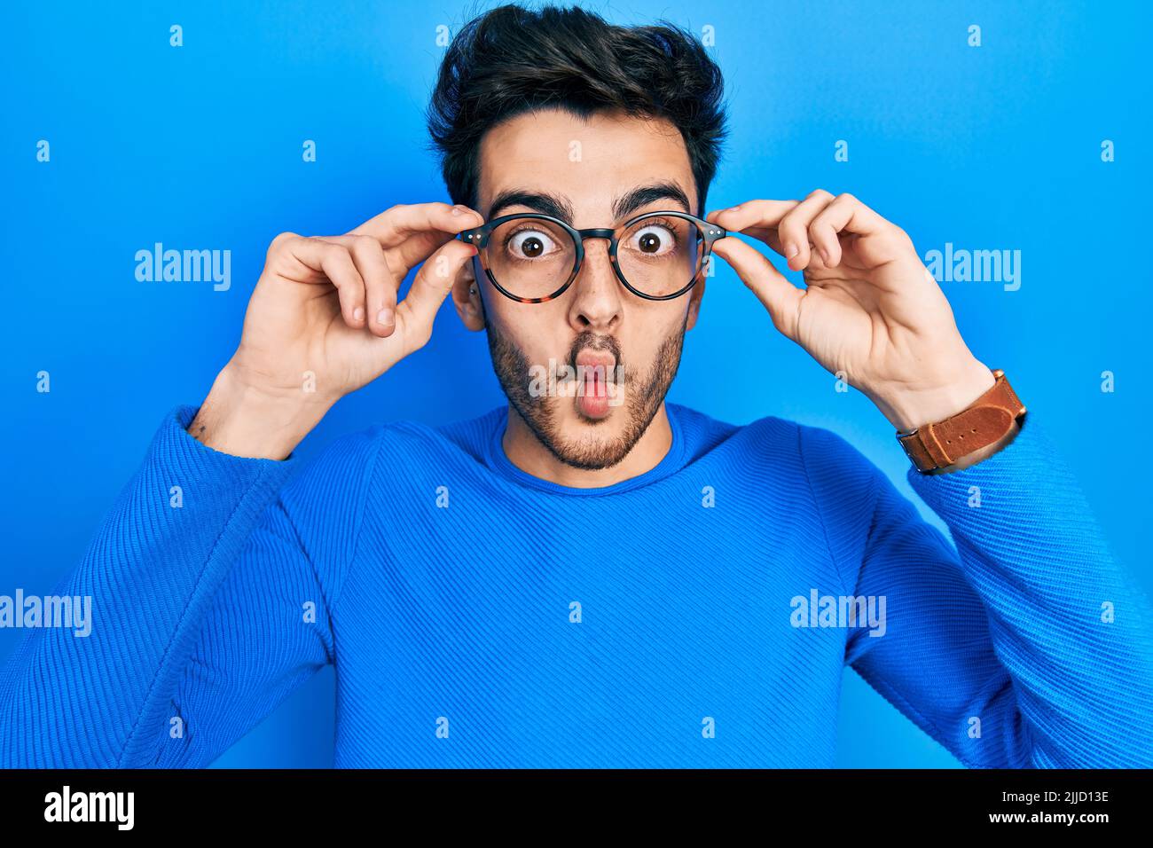 Young hispanic man wearing glasses making fish face with mouth and