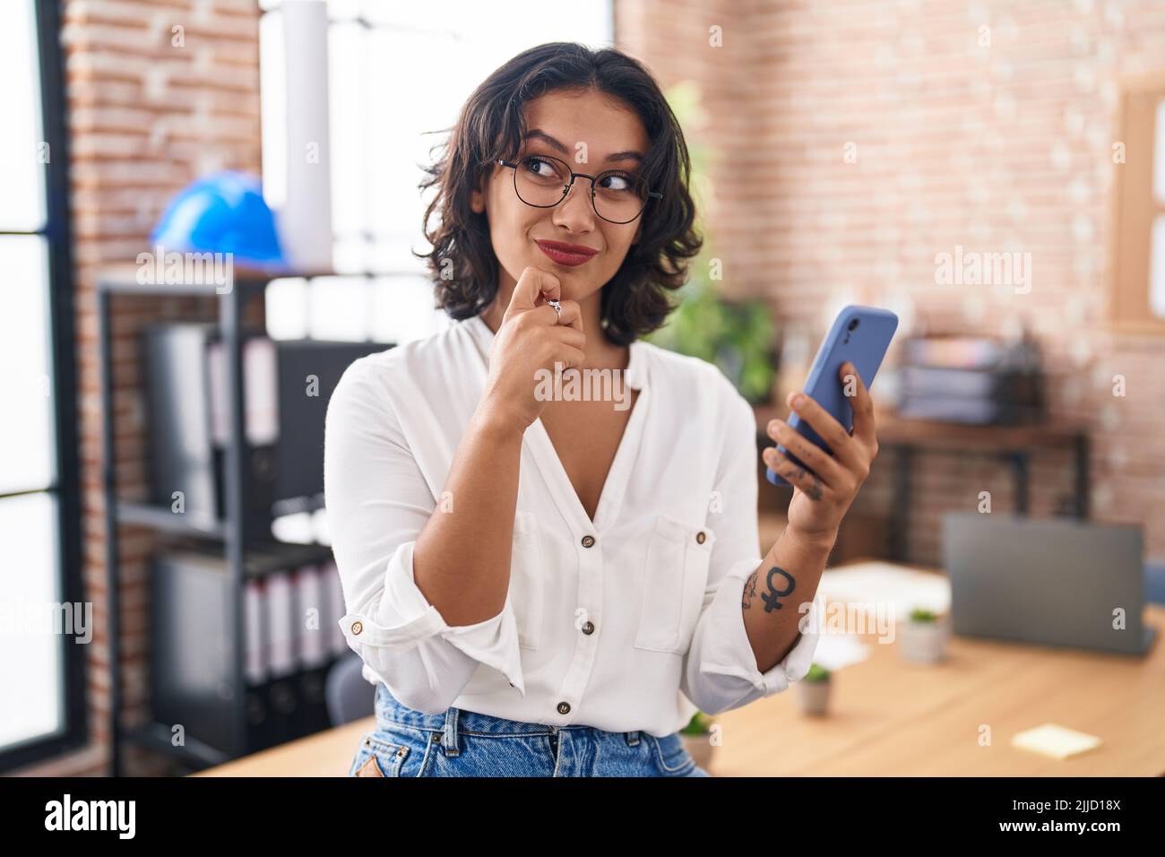 Young hispanic woman working at the office using smartphone serious ...