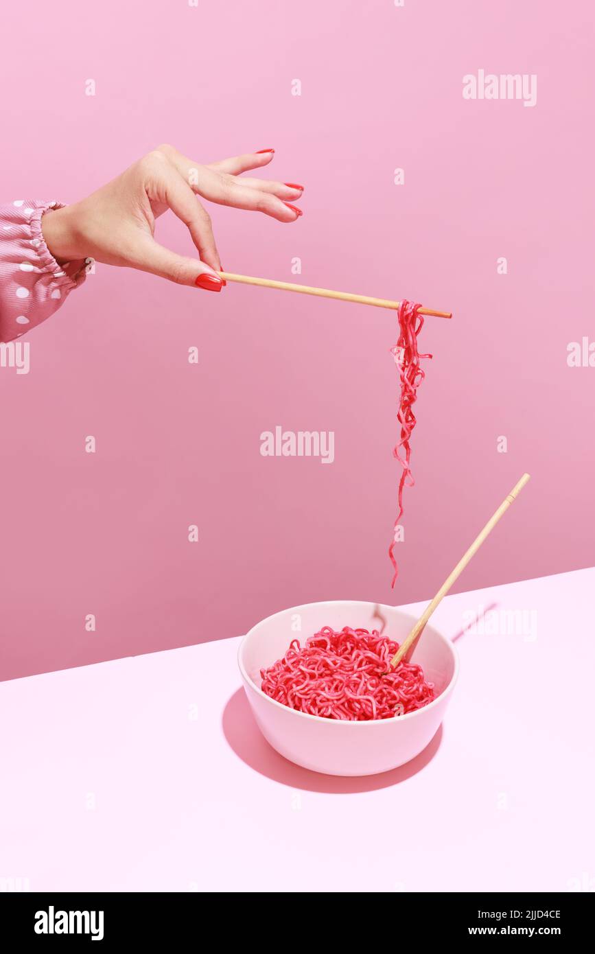 Colorful image of female hand and pink noodles isolated over pink background. Japanese cuisine