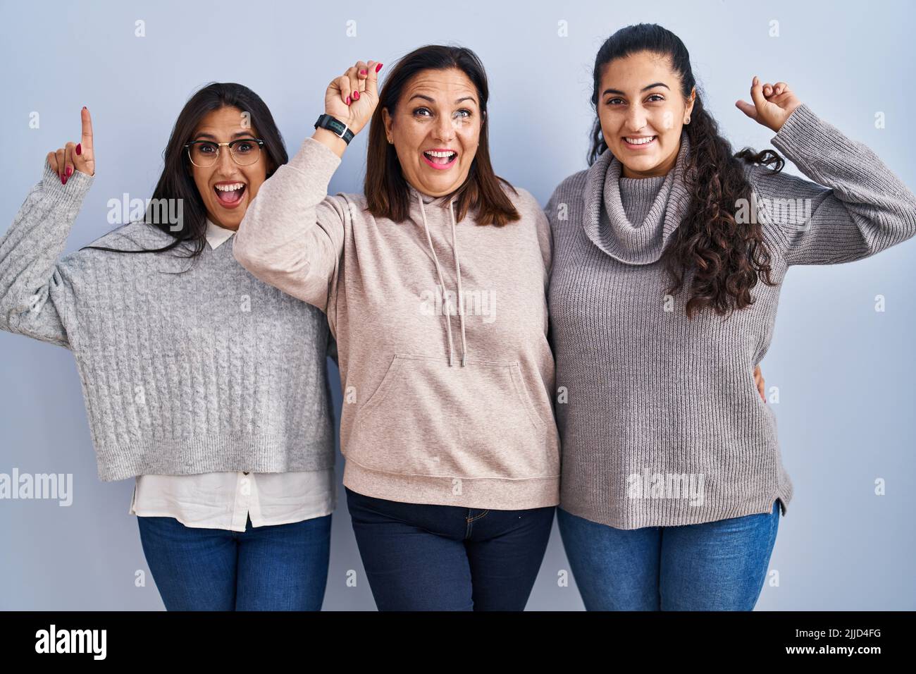 Mother and two daughters standing over blue background smiling amazed ...