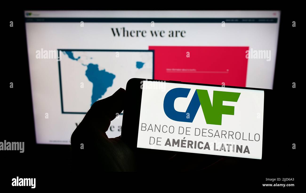 Person holding smartphone with logo of Corporacion Andina de Fomento (CAF) on screen in front of website. Focus on phone display. Stock Photo