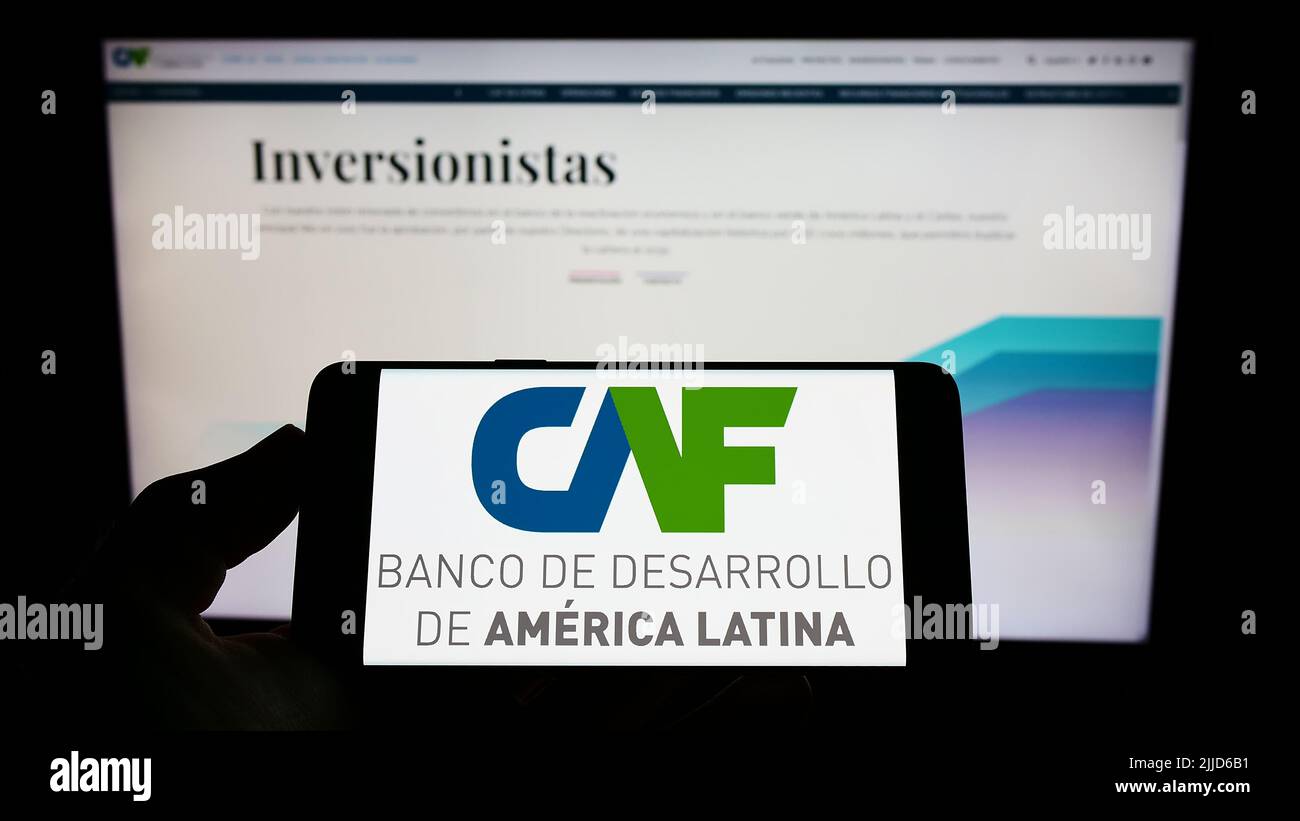 Person holding mobile phone with logo of Corporacion Andina de Fomento (CAF) on screen in front of web page. Focus on phone display. Stock Photo