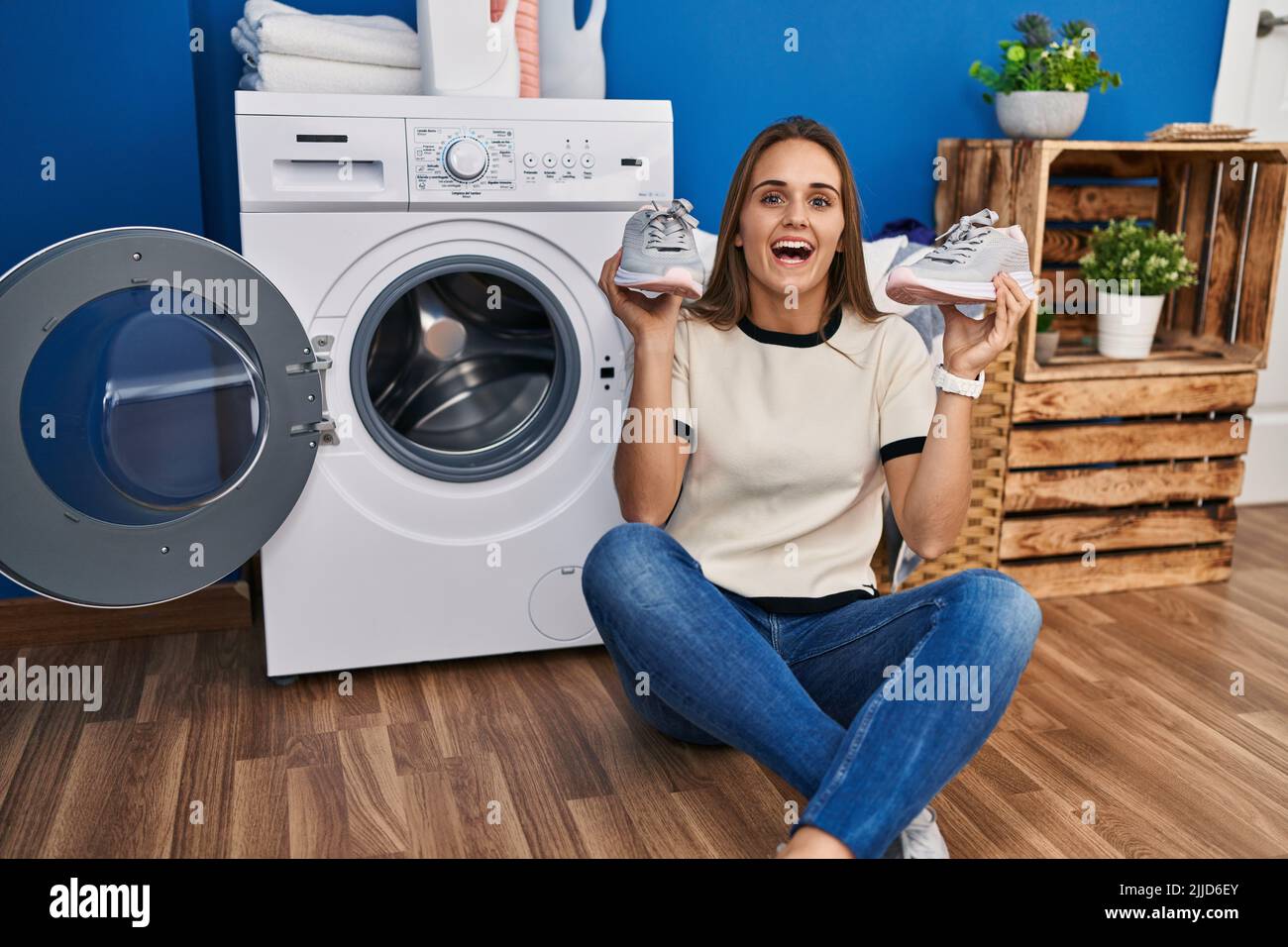 Young woman putting sneakers in washing machine celebrating crazy and