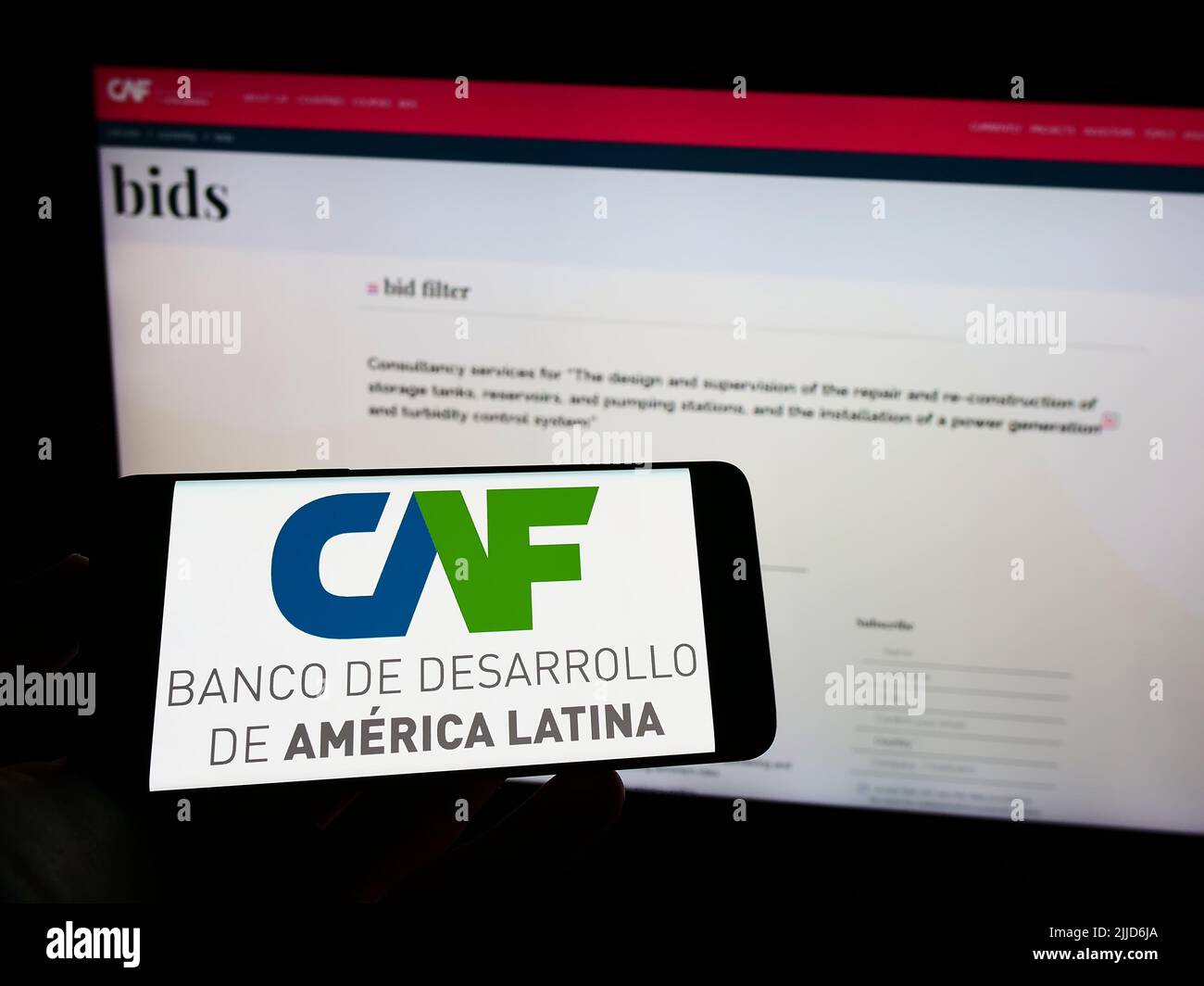 Person holding cellphone with logo of Corporacion Andina de Fomento (CAF) on screen in front of business webpage. Focus on phone display. Stock Photo