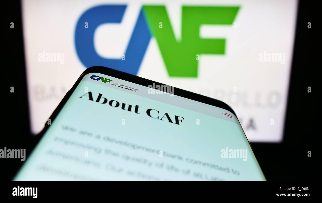 Mobile phone with website of Corporacion Andina de Fomento (CAF) on screen in front of logo. Focus on top-left of phone display. Stock Photo