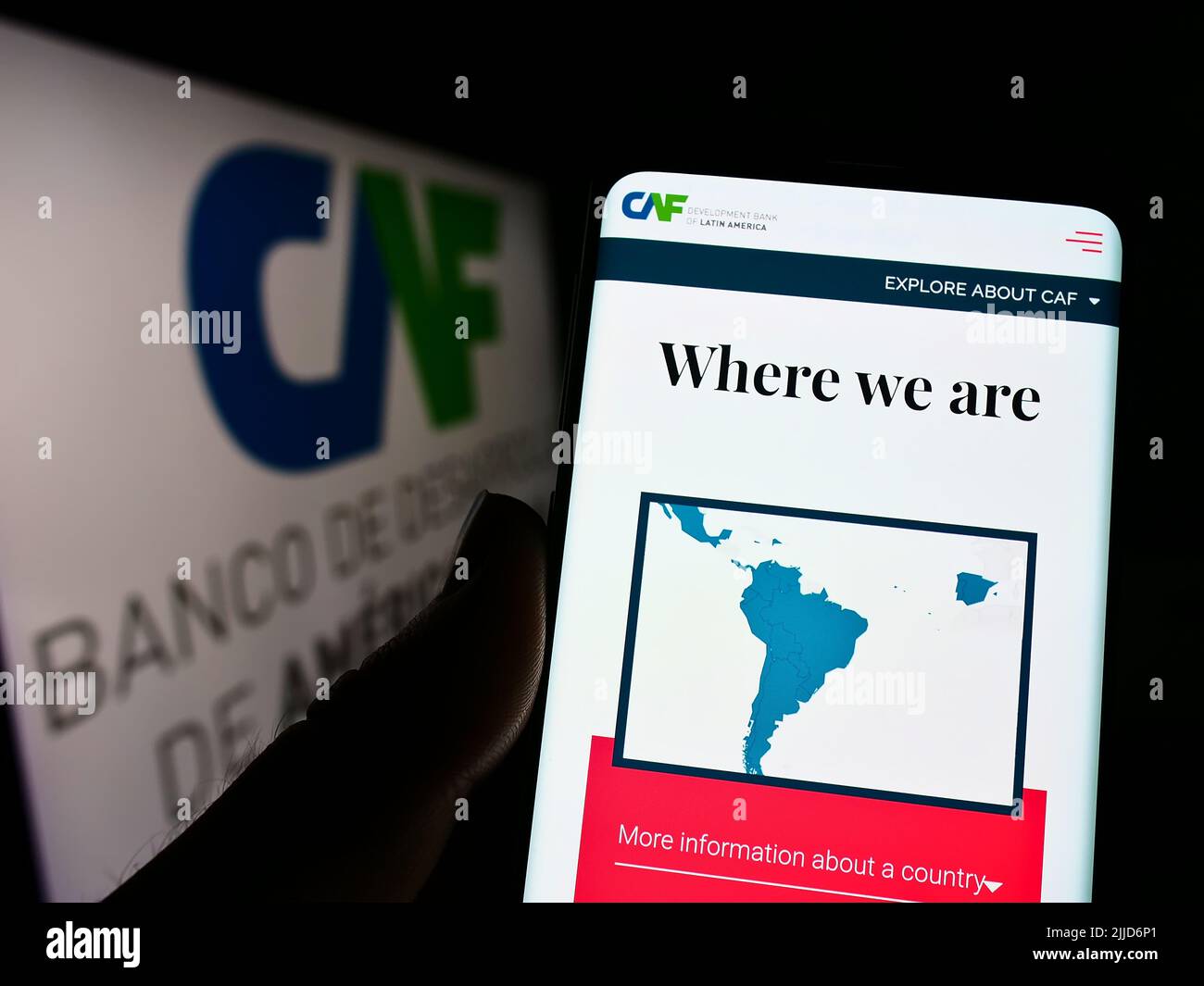 Person holding smartphone with webpage of Corporacion Andina de Fomento (CAF) on screen in front of logo. Focus on center of phone display. Stock Photo