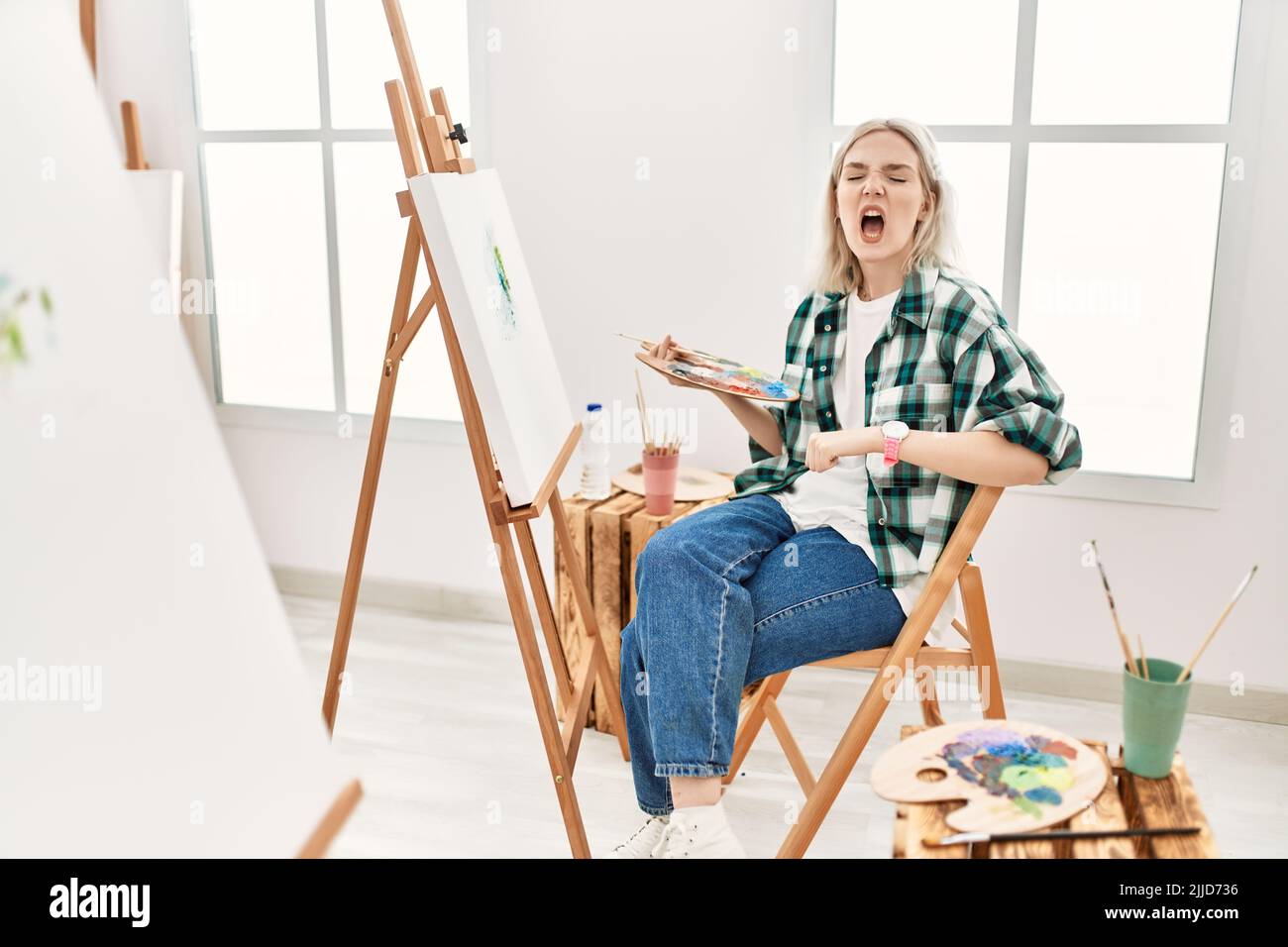 Young artist woman painting on canvas at art studio angry and mad