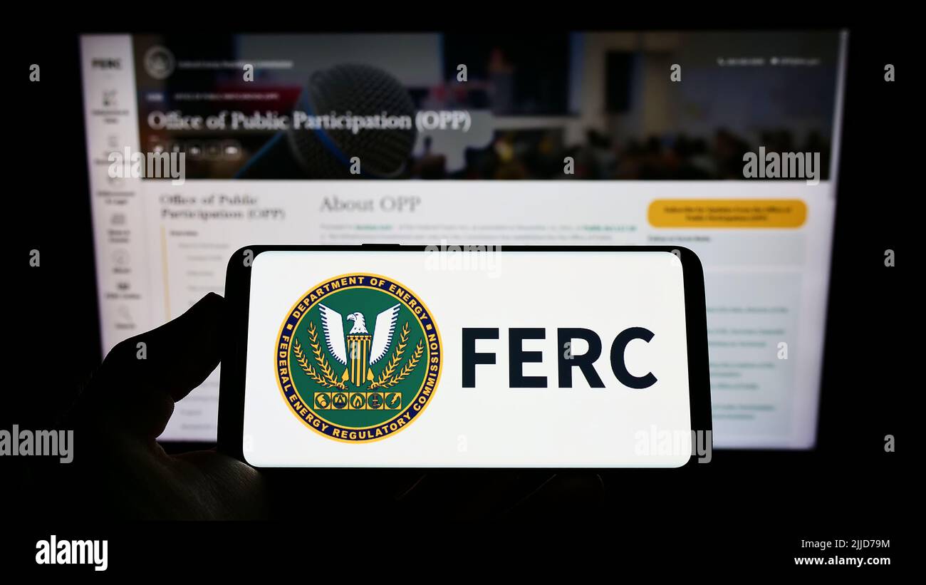 Person holding smartphone with logo of US Federal Energy Regulatory Commission (FERC) on screen in front of website. Focus on phone display. Stock Photo