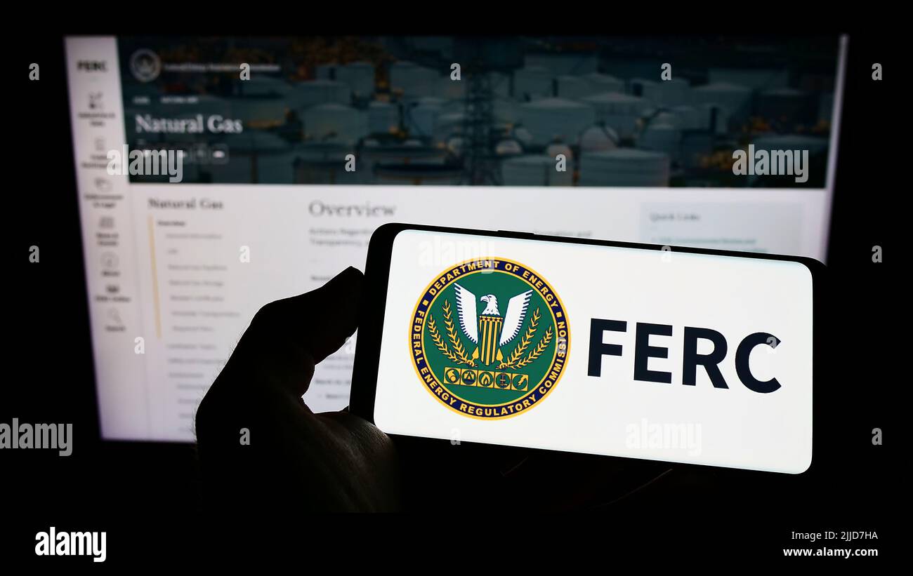 Person holding cellphone with logo of US Federal Energy Regulatory Commission (FERC) on screen in front of webpage. Focus on phone display. Stock Photo