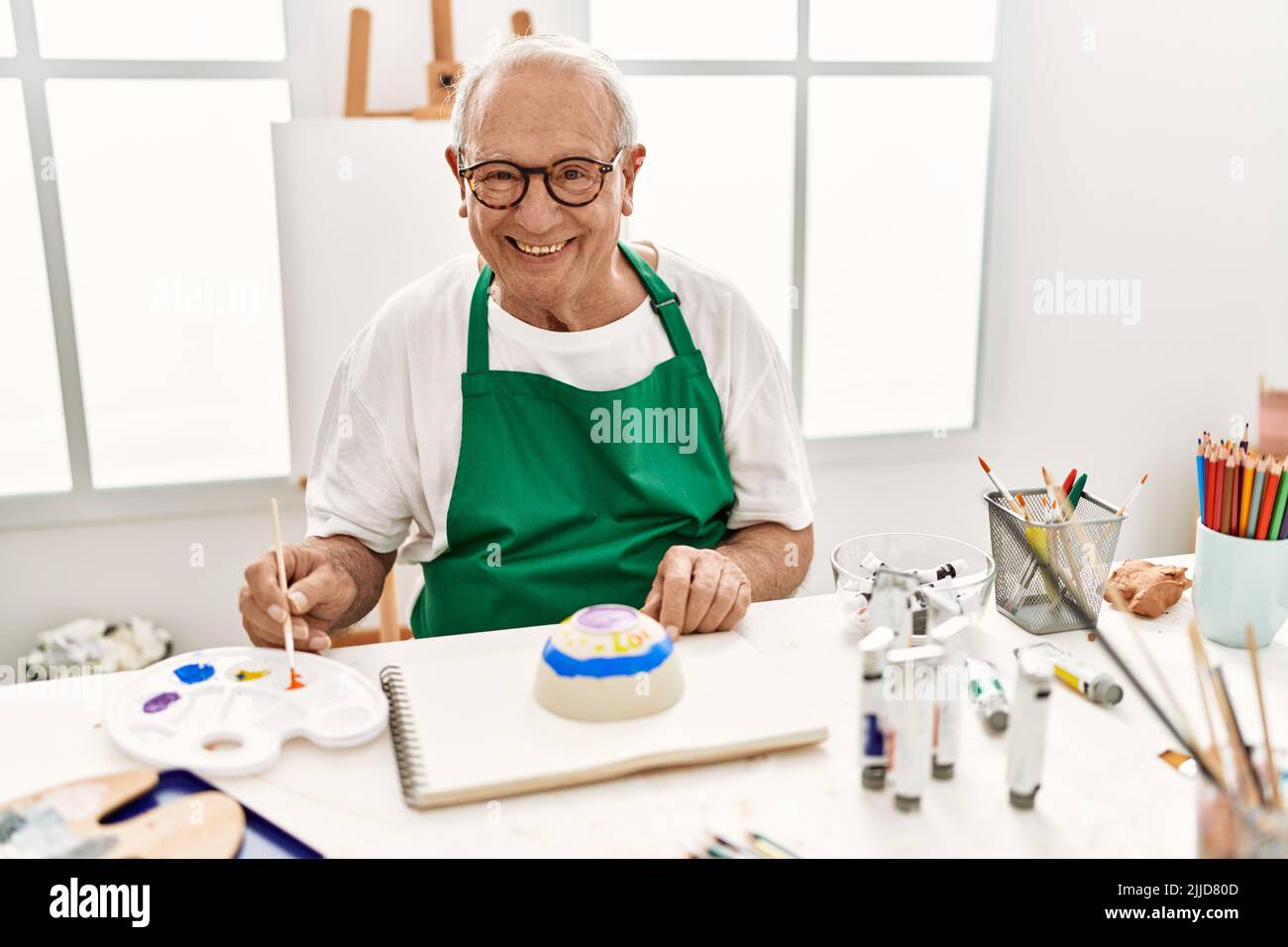 Senior grey-haired artist man smiling happy painting pottery sitting on ...