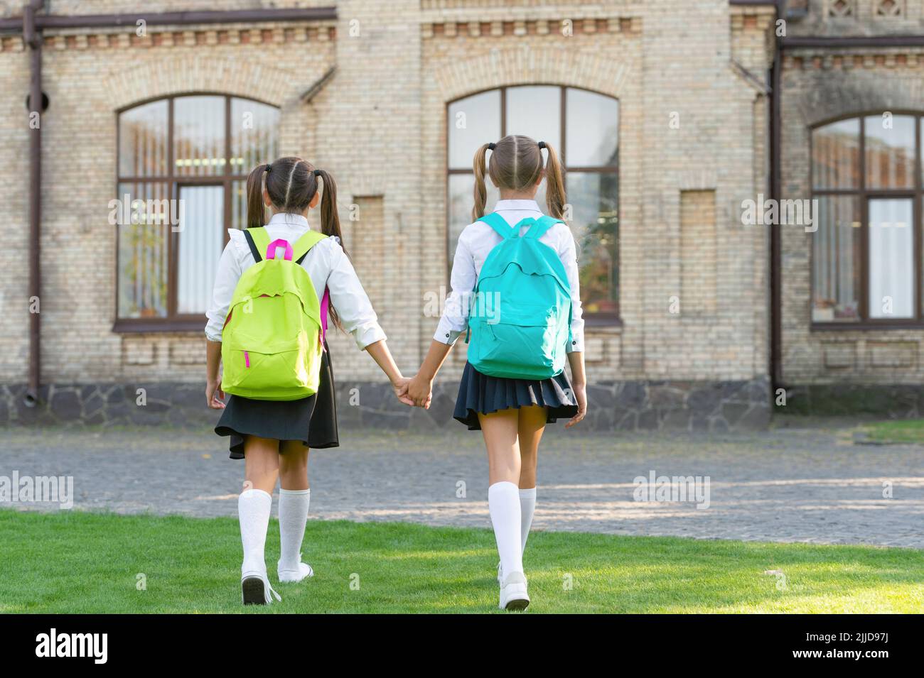 back view of two girls with school backpack walking together outdoor ...