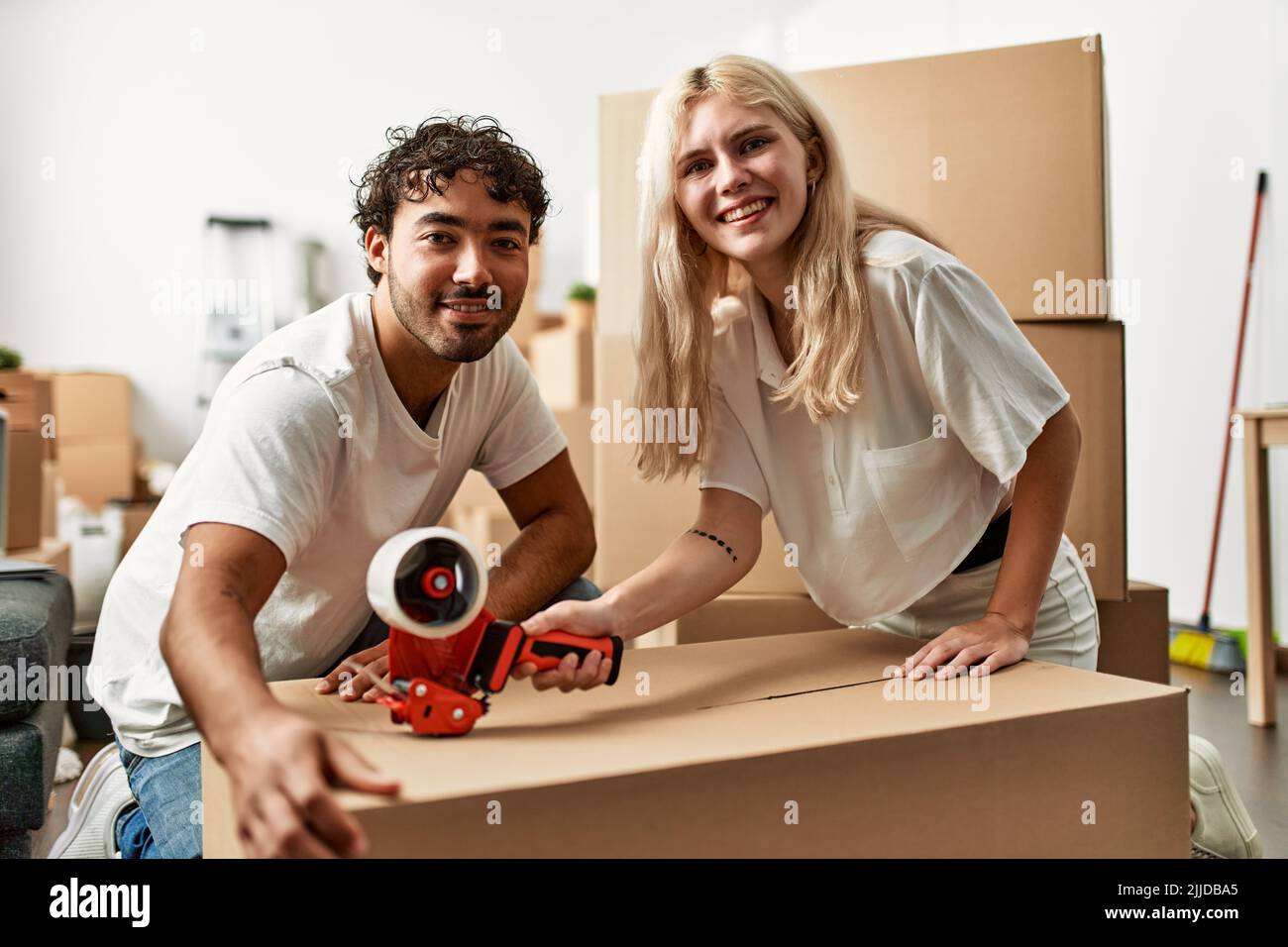 Young beautiful couple smiling happy packing cardboard box at new home ...