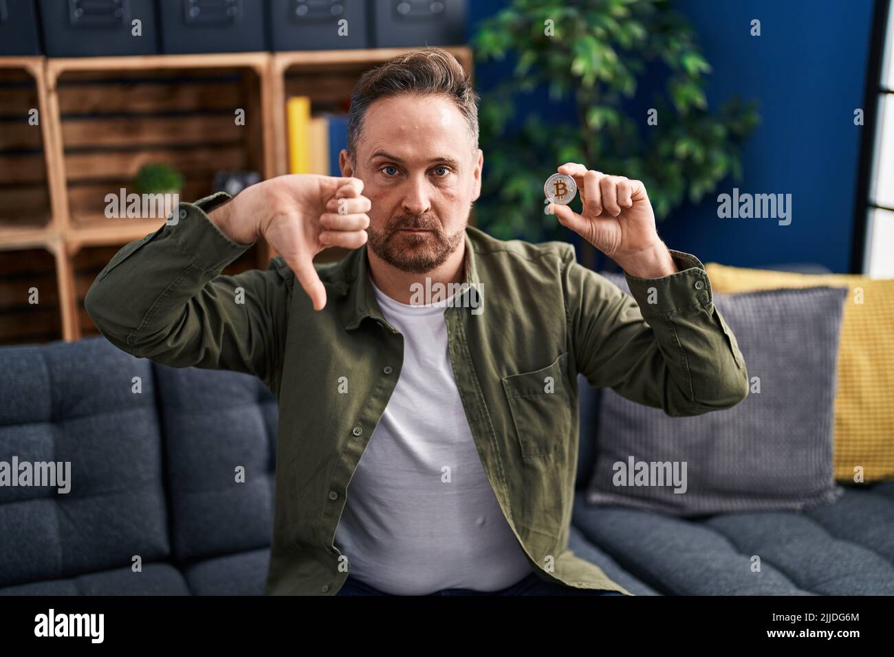 Middle age caucasian man holding virtual currency bitcoin with angry ...