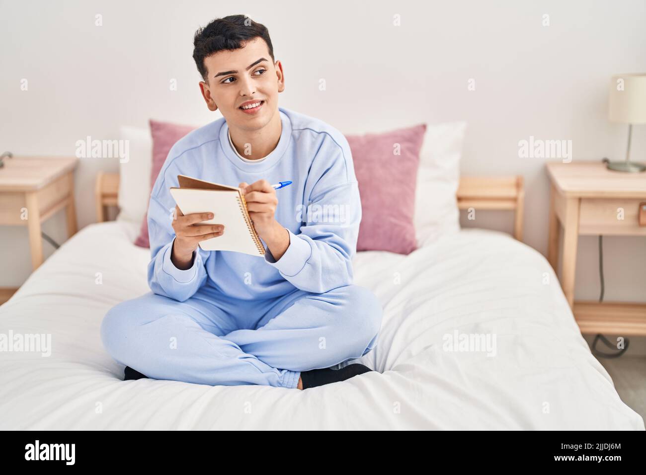 Young non binary man writing on notebook sitting on bed Stock Photo - Alamy