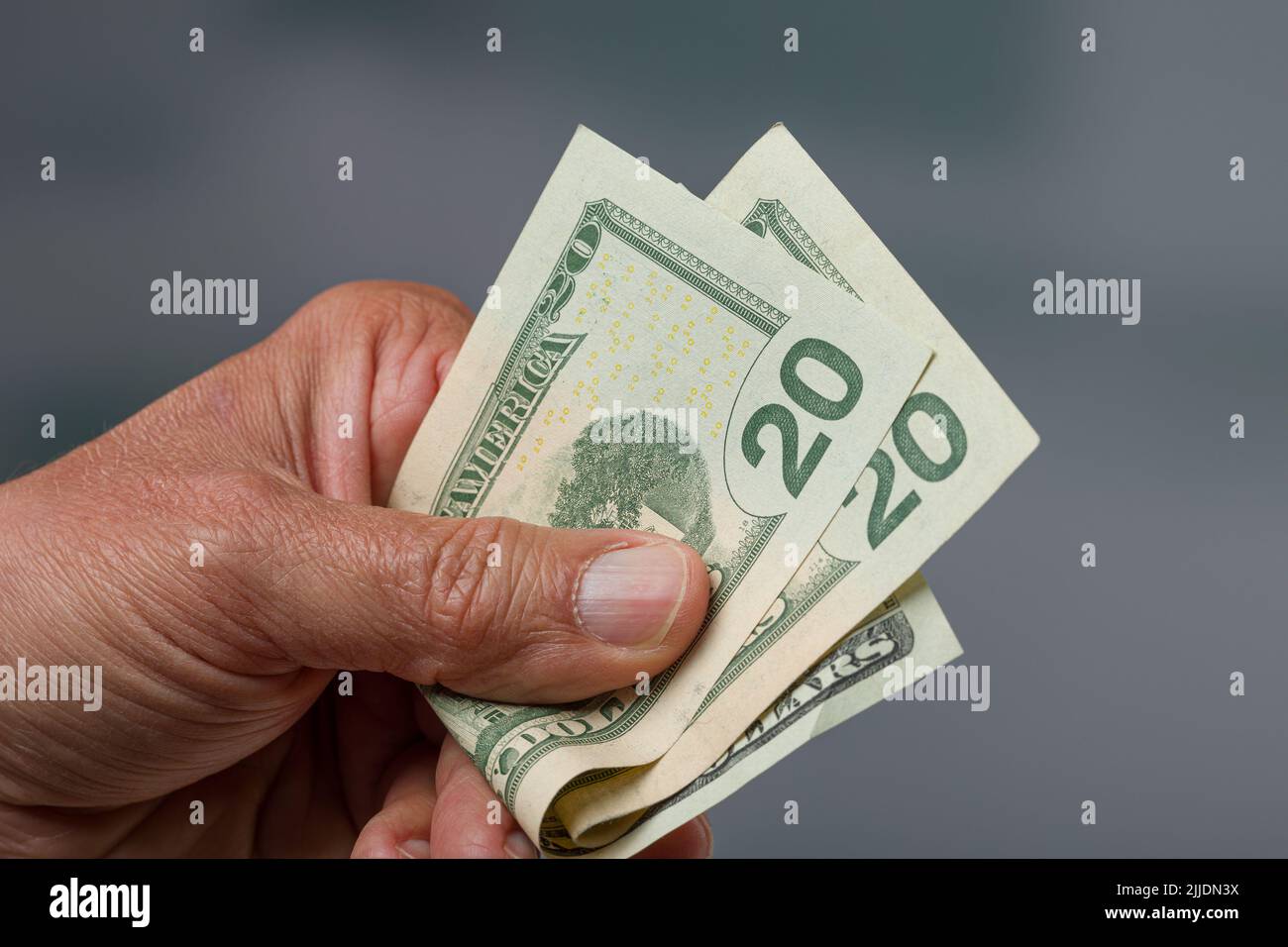 close-up of a man's hand holding a bunch of twenty dollar bills / greenbacks Stock Photo