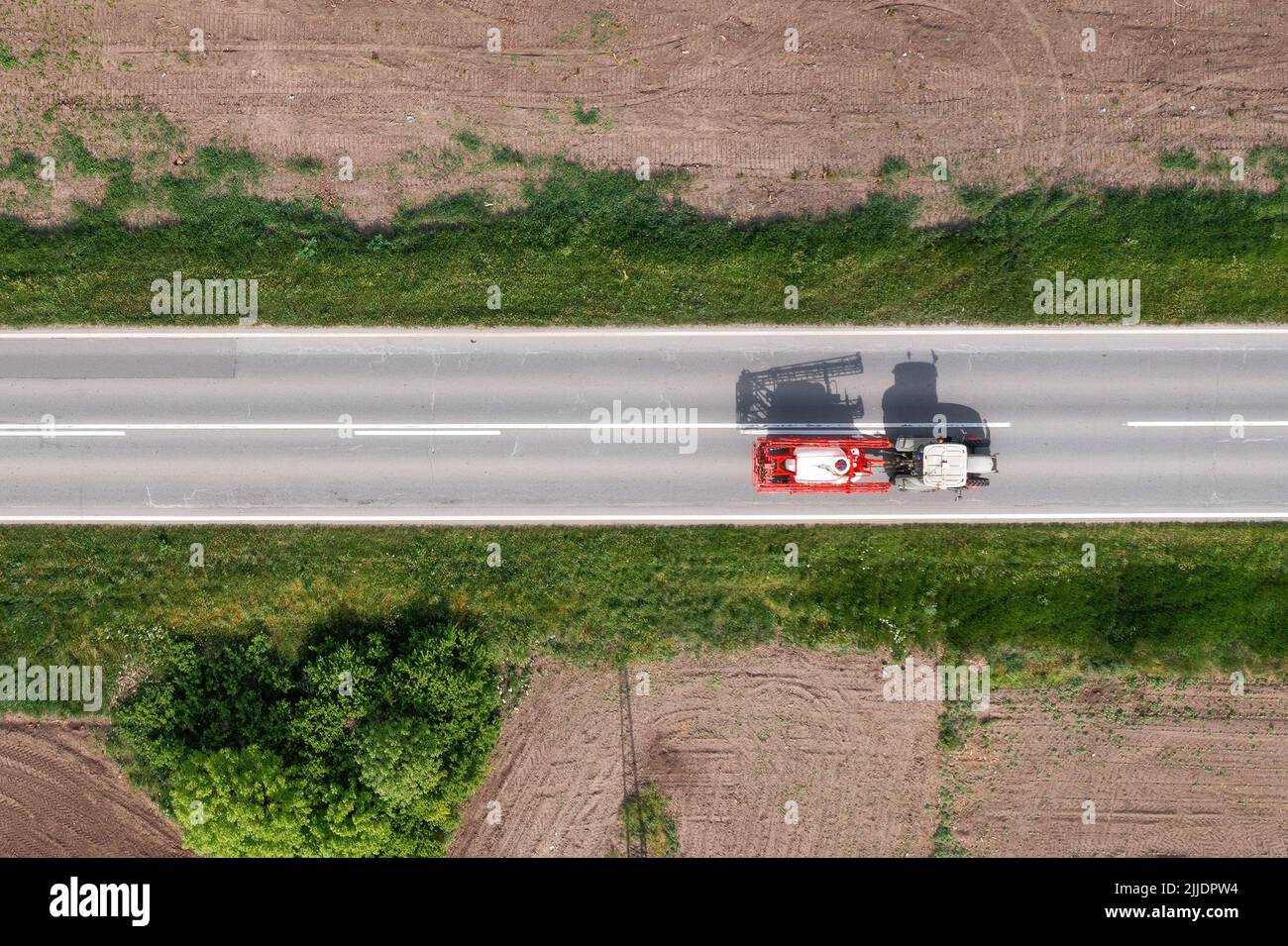 Agricultural tractor with crop sprayer attached driving along the road through countryside landscape, drone pov directly above aerial shot in agricult Stock Photo