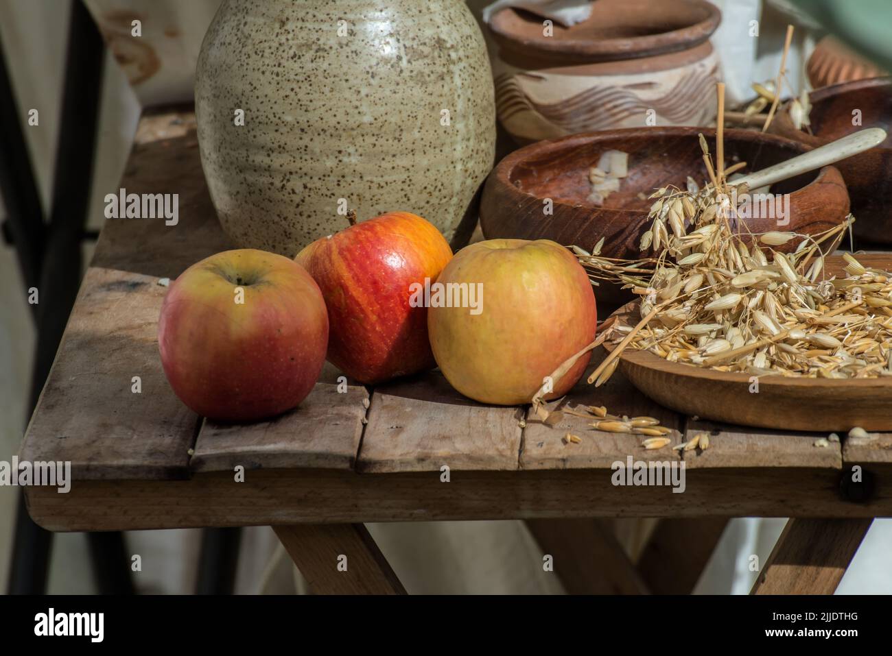 Three apples and a bowl of wheat grain with some pots on a wooden table Stock Photo