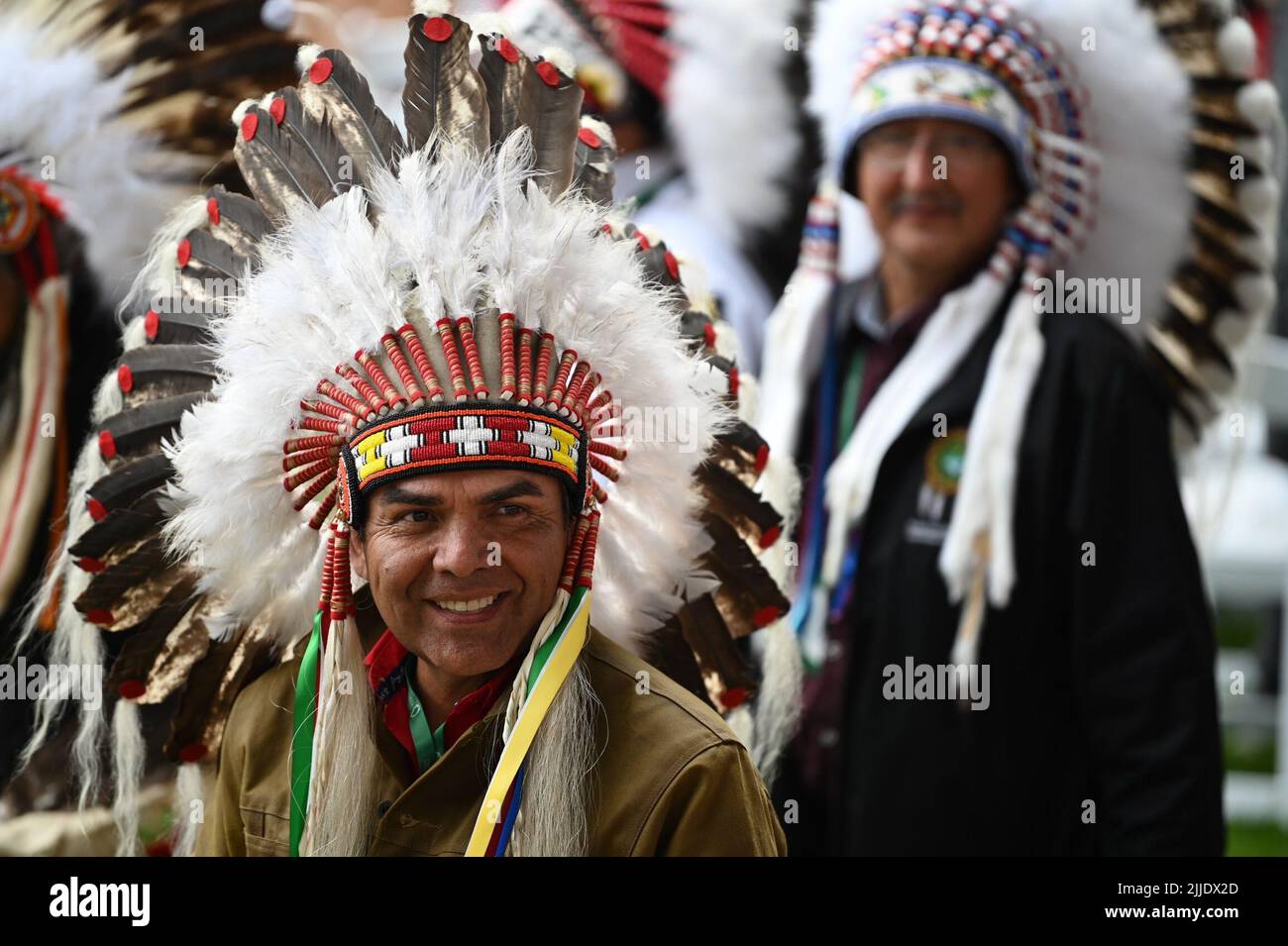 Maskwacis, Canada. 25th July, 2022. A Canadian native wearing a headdress smiles during Pope Francis' visit as part of his multi-day trip to Canada. Francis is visiting Canada to meet with the country's indigenous people, whose family members once suffered abuse, violence and humiliation in church-run boarding schools. Credit: Johannes Neudecker/dpa/Alamy Live News Stock Photo