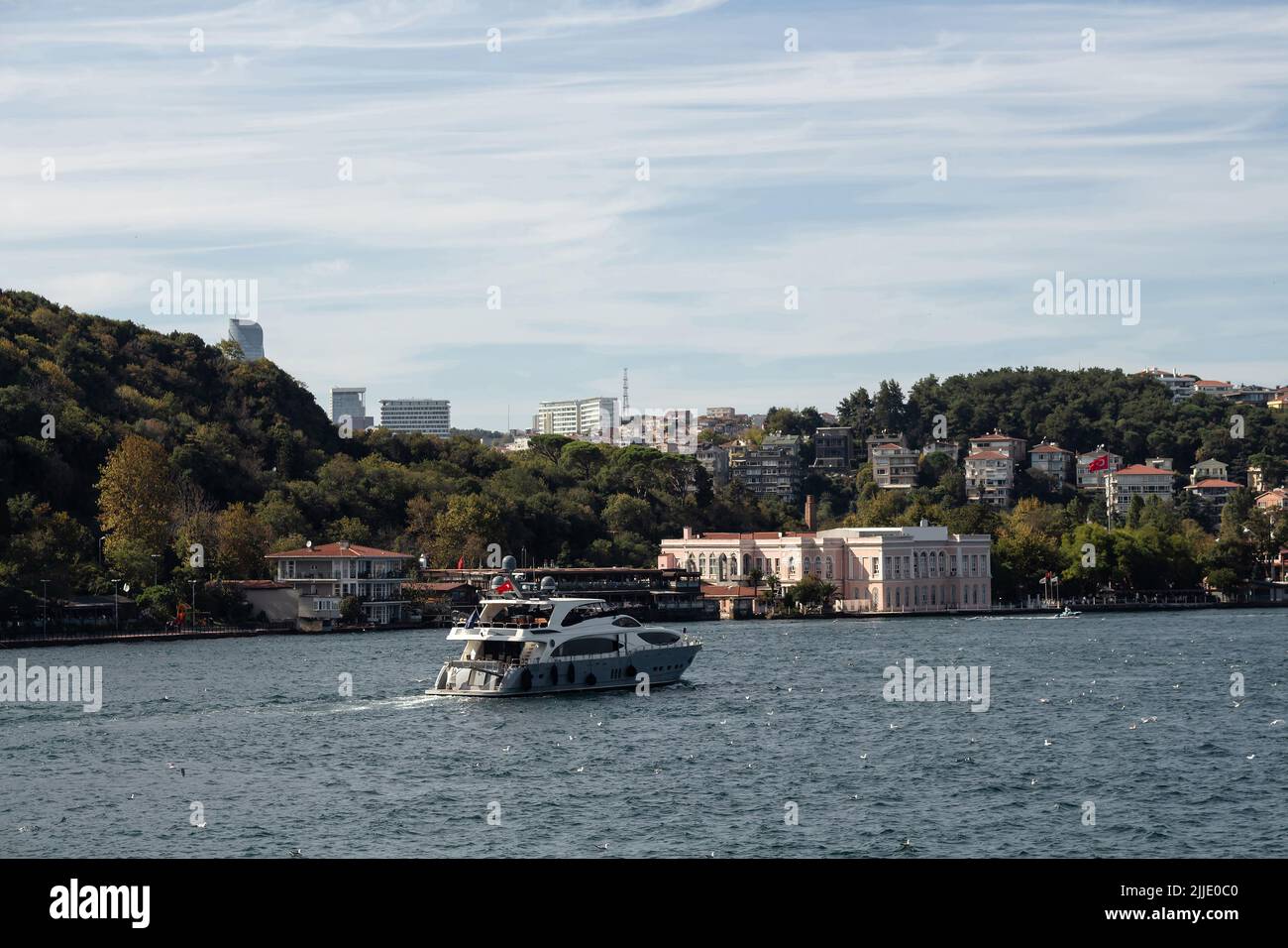 View of a yacht passing on Bosphorus and Baltalimani neighborhood on European side of Istanbul. It is a sunny summer day. Beautiful travel scene. Stock Photo