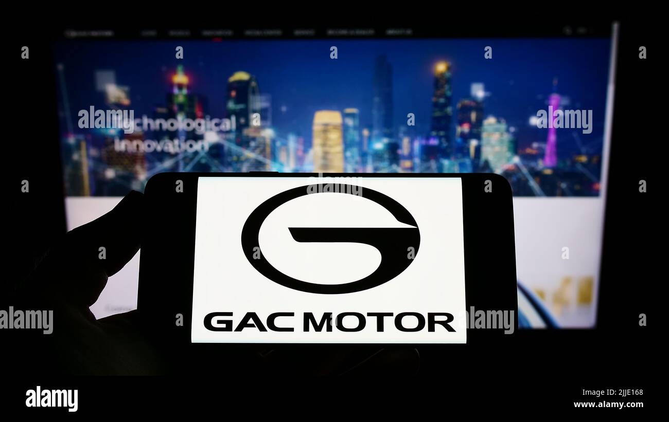 Person holding smartphone with logo of Guangzhou Automobile Group Co., Ltd. (GAC) on screen in front of company website. Focus on phone display. Stock Photo