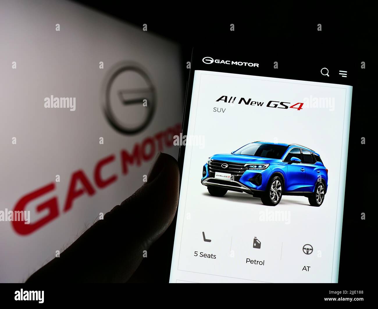 Person holding cellphone with webpage of Guangzhou Automobile Group Co., Ltd. (GAC) on screen in front of logo. Focus on center of phone display. Stock Photo