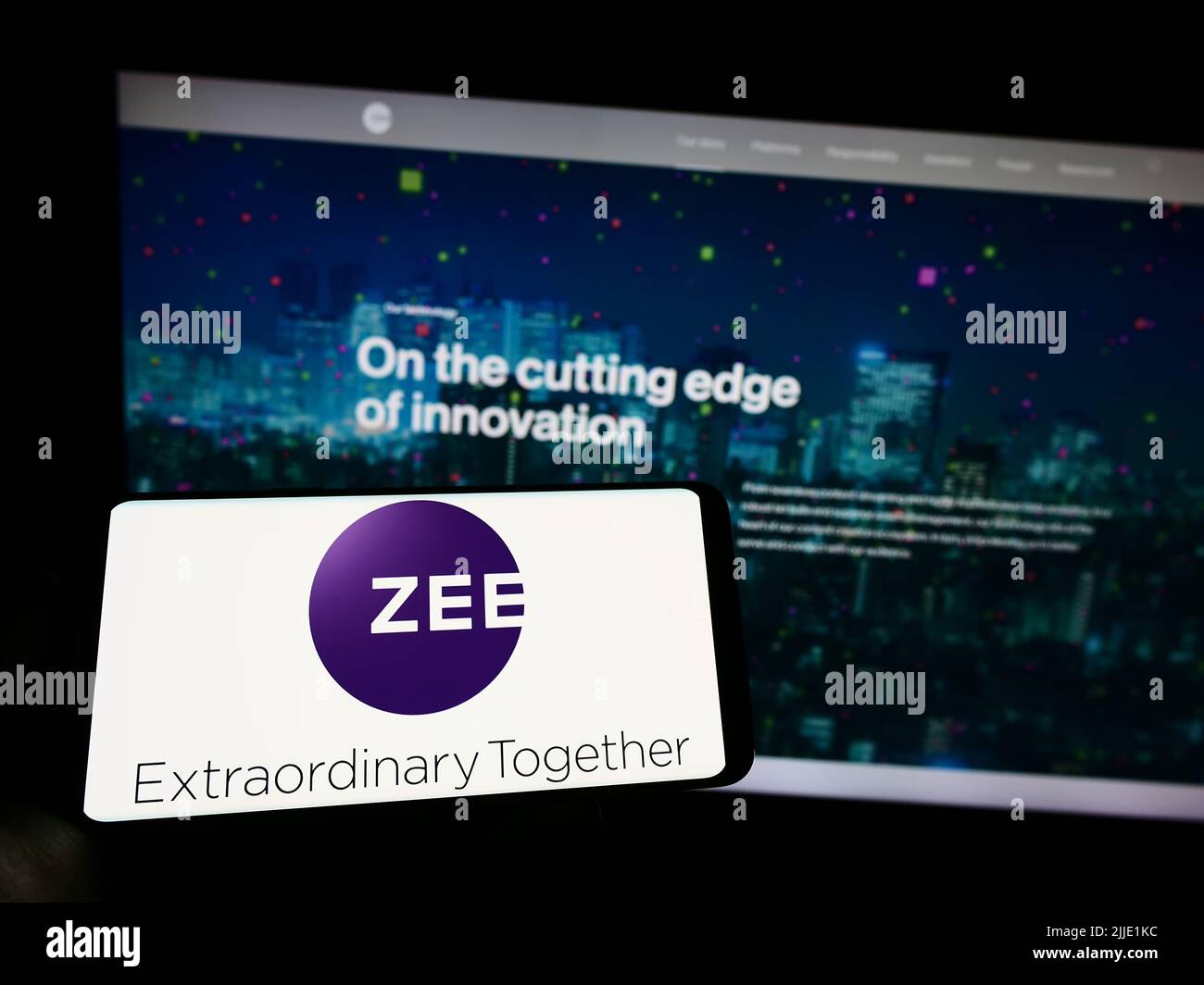 Person holding cellphone with logo of company Zee Entertainment Enterprises Ltd. on screen in front of business webpage. Focus on phone display. Stock Photo