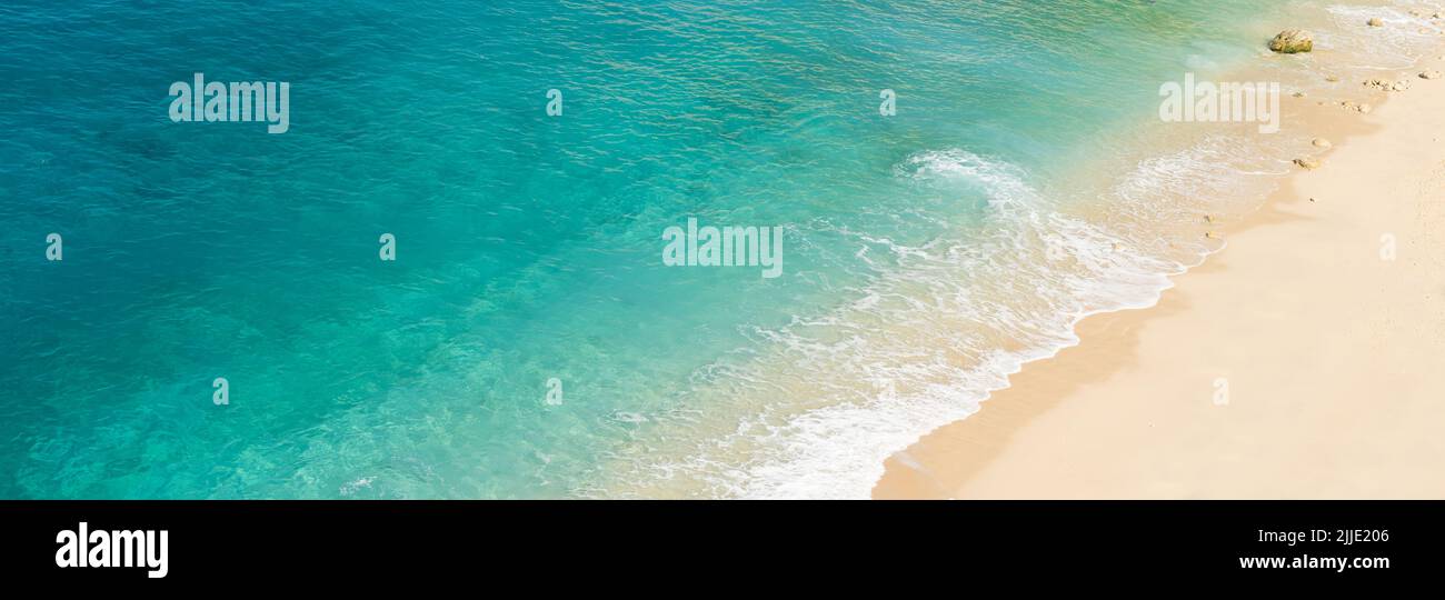 Panoramic photo of  beach with blue and green toned crystal clear sea and sand as a luxury summer holiday background or backdrop. Stock Photo