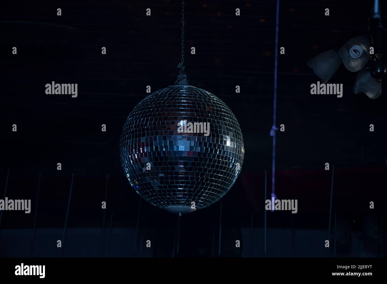 A closeup of a shiny disco ball hanging on a metal string in a dark ...