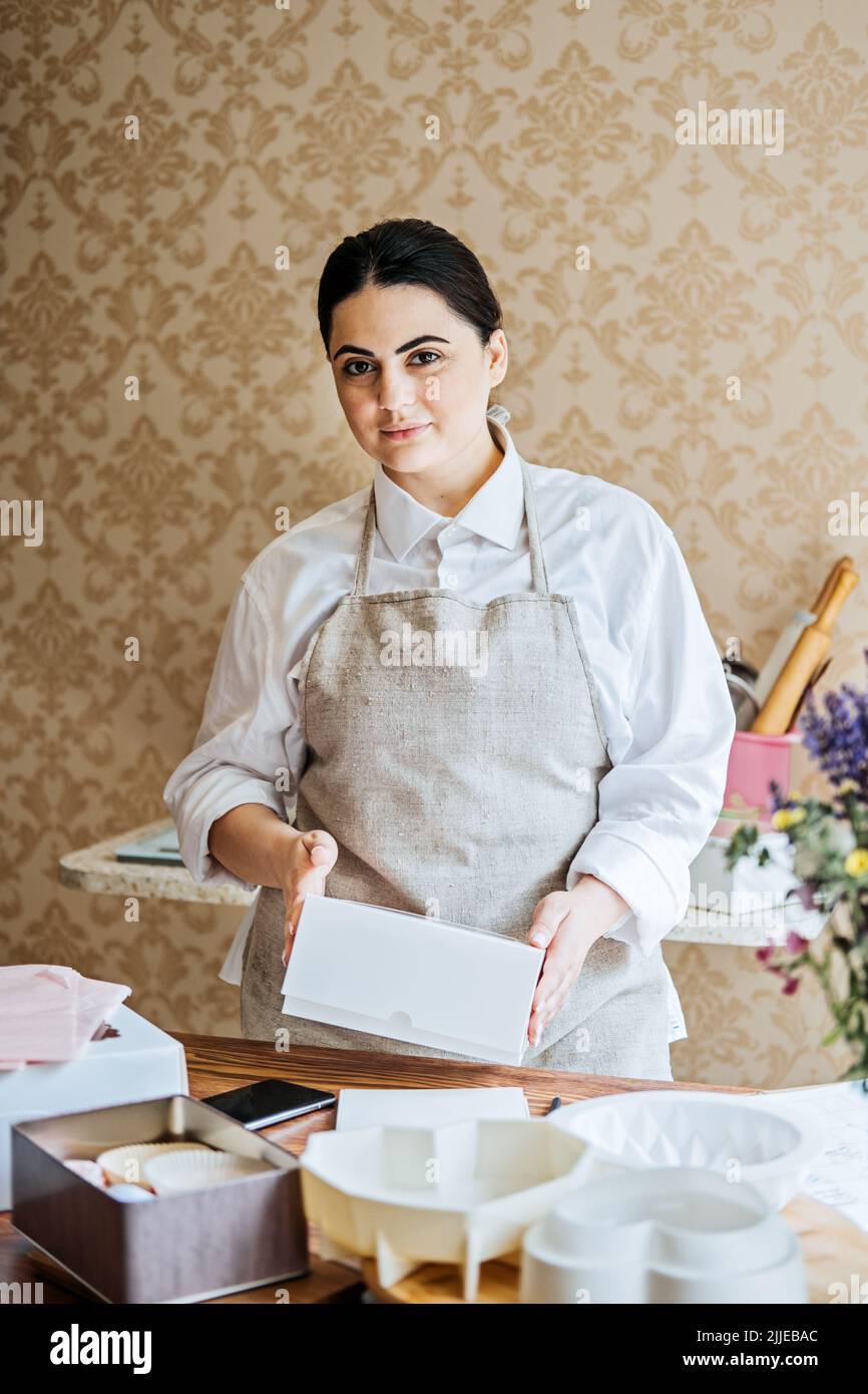 Female baker, pastry chef preparing cake order. Arabic Asian woman