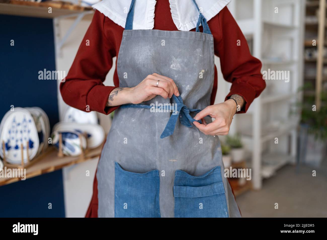 Female ceramist tying her apron before working with raw clay in pottery
