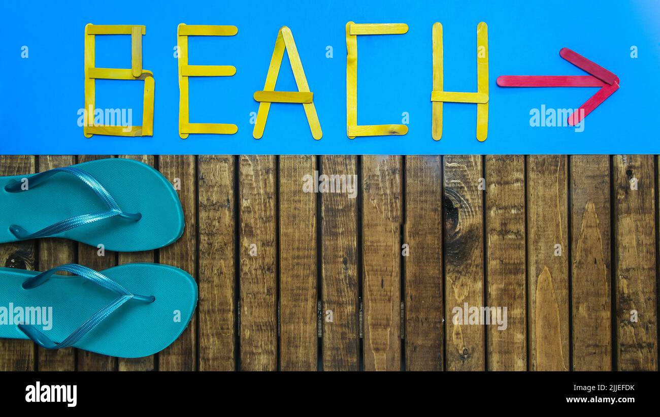 Background with flip flops on wood  and text beach on blue with arrow background Stock Photo