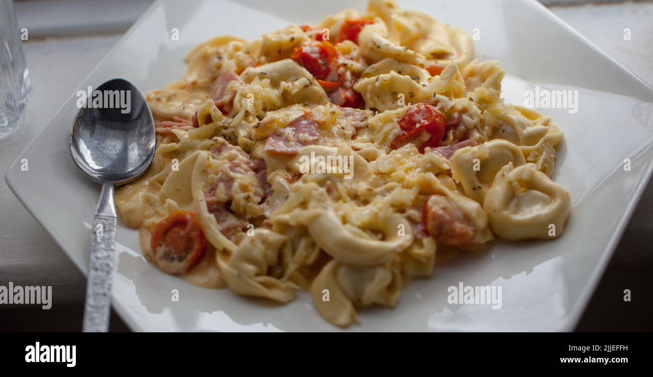 Creamy Three Cheese Tortellini with tasty cherry tomatoes and parma ham Stock Photo