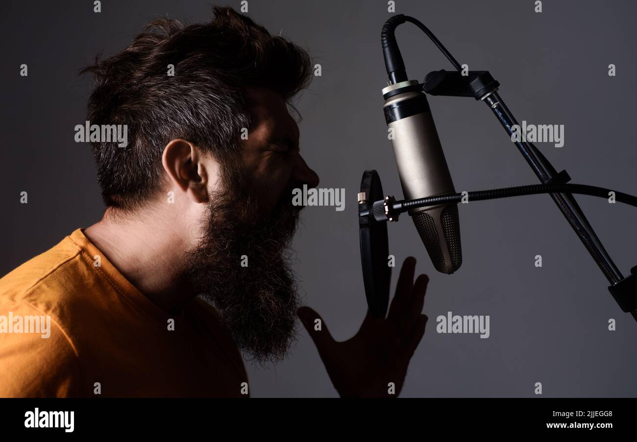 Emotional bearded man singing to condenser microphone in studio. Professional male vocalist. Music. Stock Photo