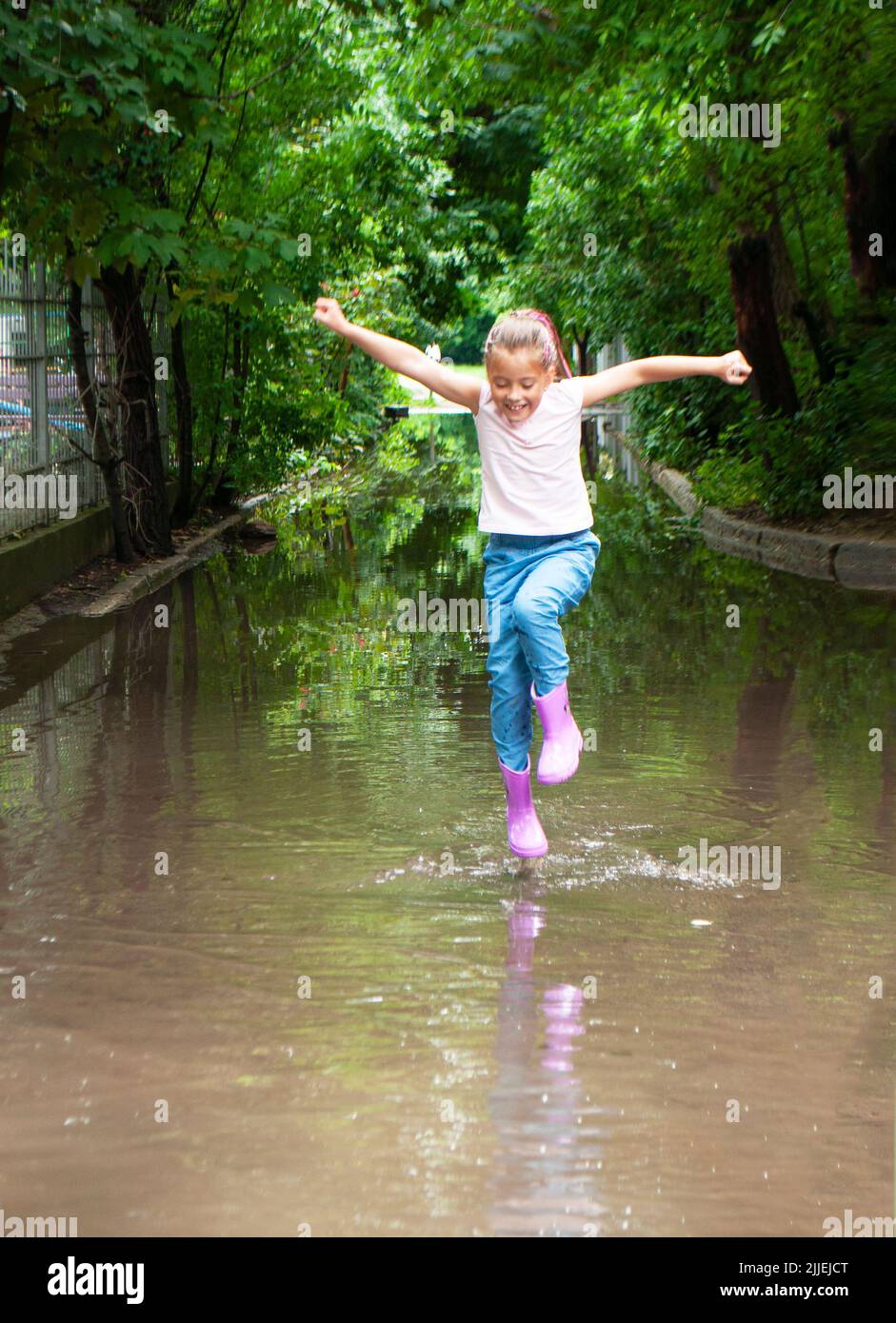 A happy braided girl in rubber boots is jumping in muddy puddles Stock ...