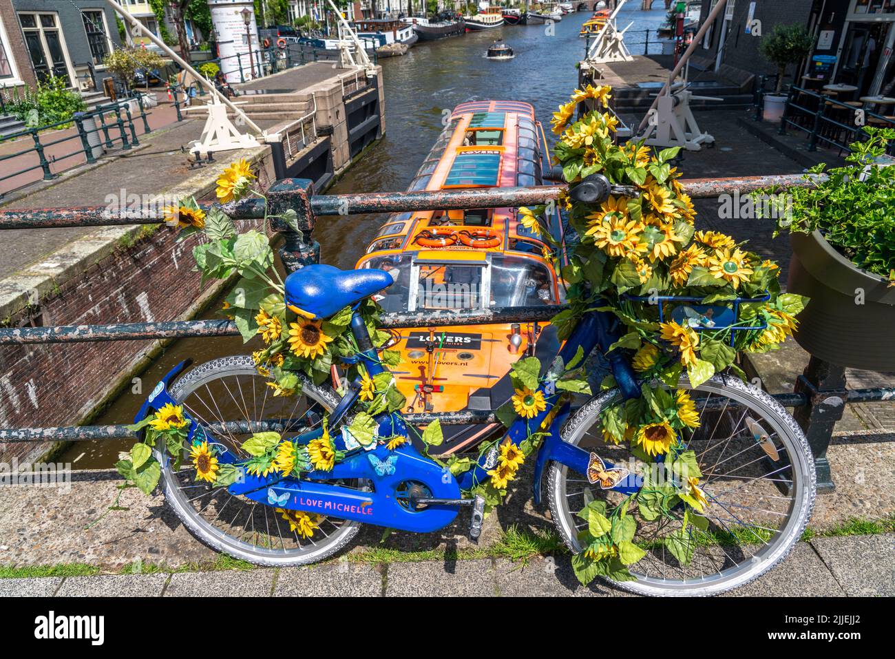 Sint Antoniesluis, on the Oudeschans canal, bicycle decorated with sunflowers, canal cruise boat, café, De Sluyswacht, Amsterdam, Netherlands Stock Photo
