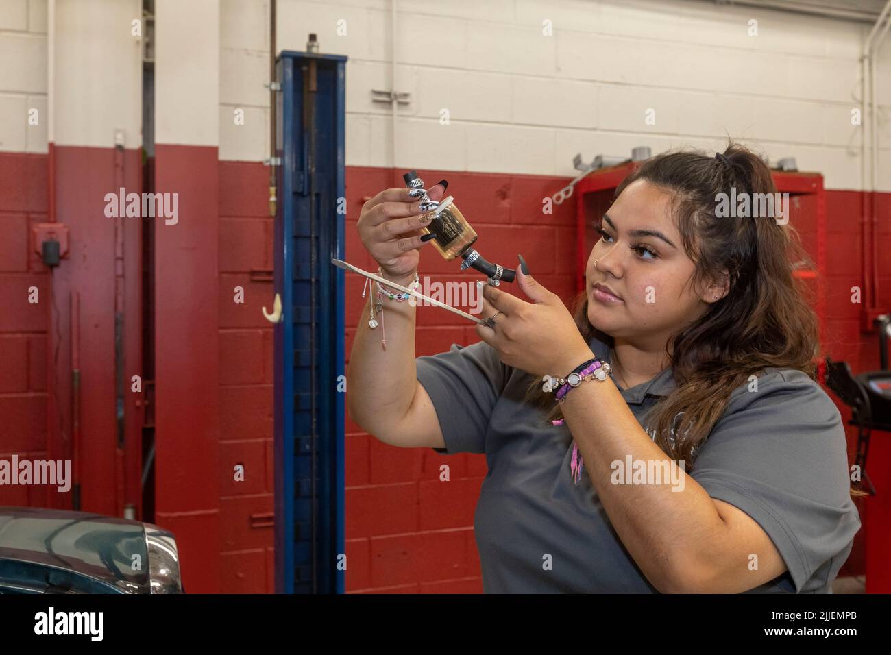 Aurora, Colorado - Cinthia Cabral examines a fuel filter she removed from a car at Hands of the Carpenter. The nonprofit repairs vehicles belonging to Stock Photo