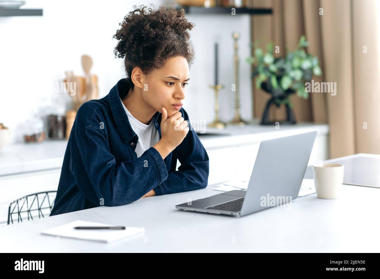 An anxious African American woman, trader, freelancer, looks worriedly at the laptop screen, monitors the situation in the financial market, concentrated analyzes the dynamics, feeling stressful Stock Photo