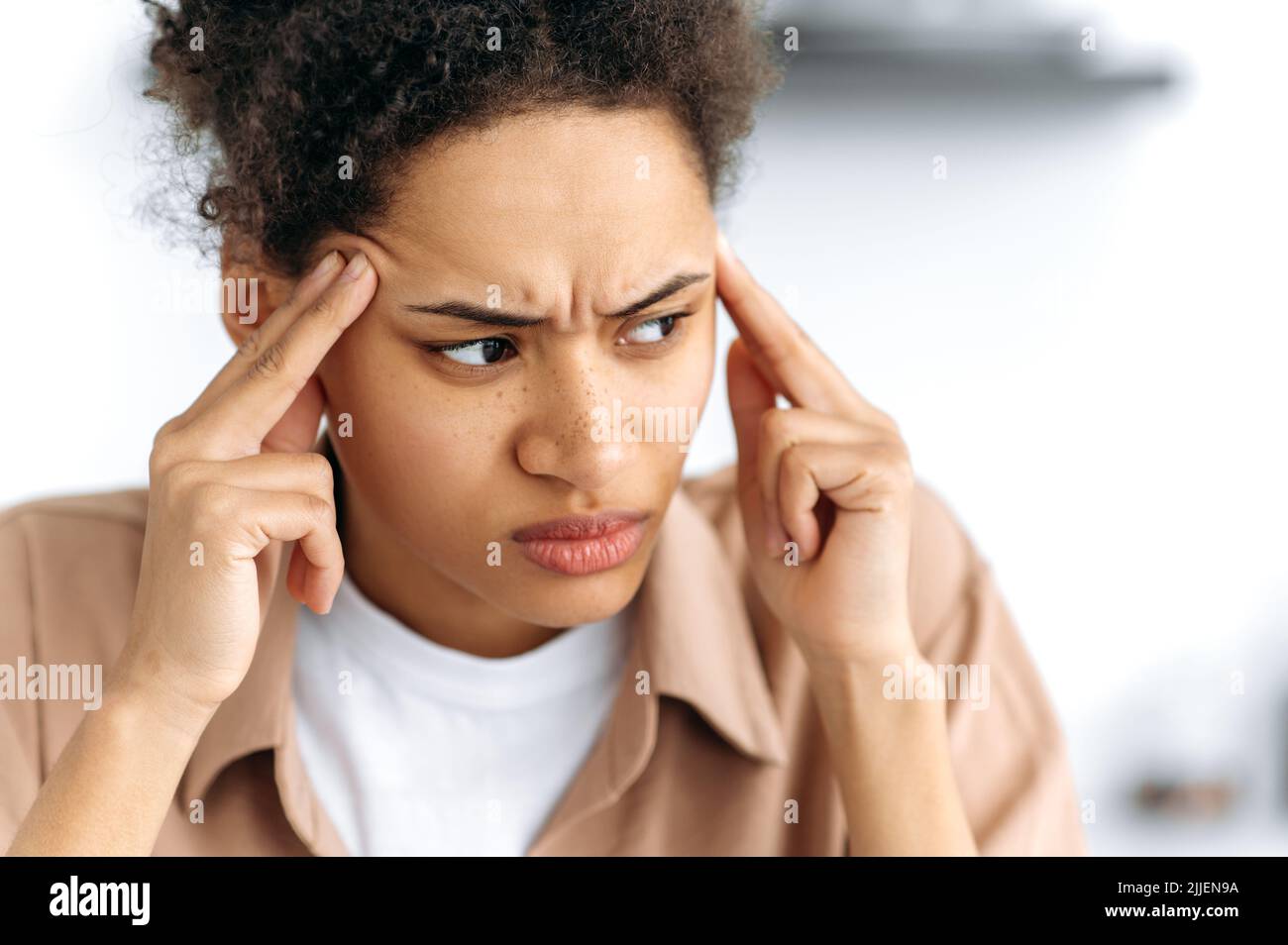 Close-up of stressful tired african american exhausted woman, experiencing fatigue from work, overwork, suffering from headache, migraine, massages her temples, looks to the side, needs rest Stock Photo