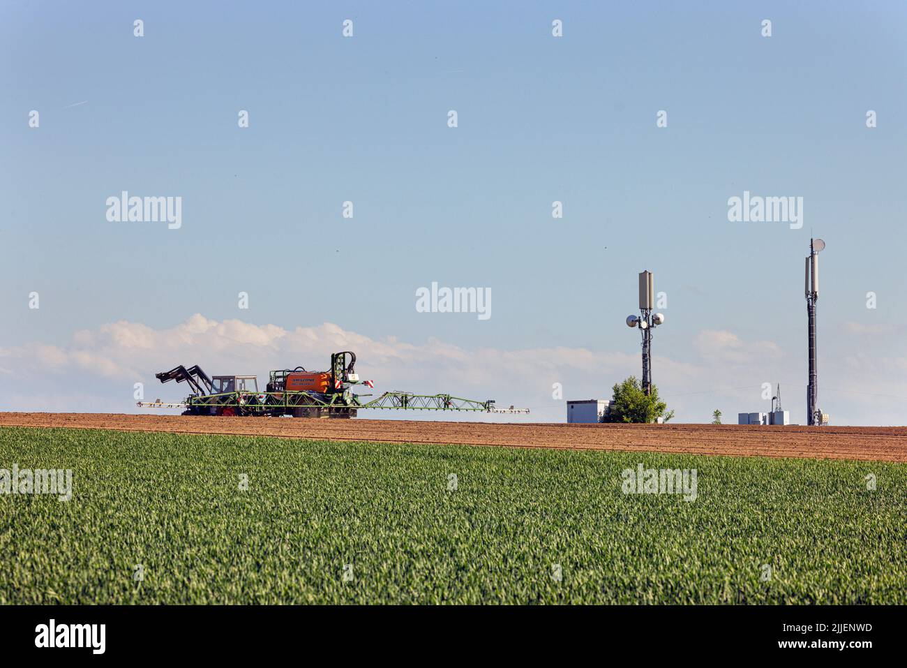 farmer spraying field with glyphosate, mobile phone masts in background, Germany, Bavaria, Erdinger Moos Stock Photo