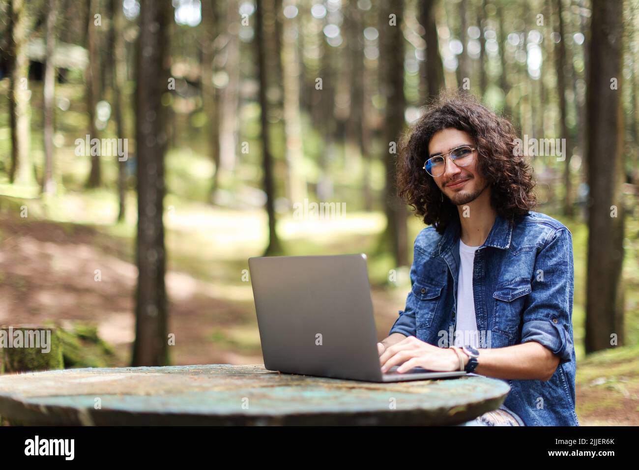 Young latin man sitting in the forest working with laptop looking camera at Costa Rica Stock Photo