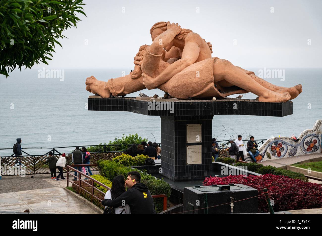 A young couple kisses in front of a public art sculpture entitled 'El Beso' (the kiss) at the Miraflores malecon on a Sunday afternoon. Stock Photo