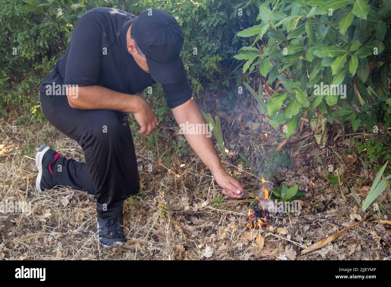 Image of a man dressed in black lighting a trigger to set fire to a forest. Reference to the problem of fires and arsonists Stock Photo