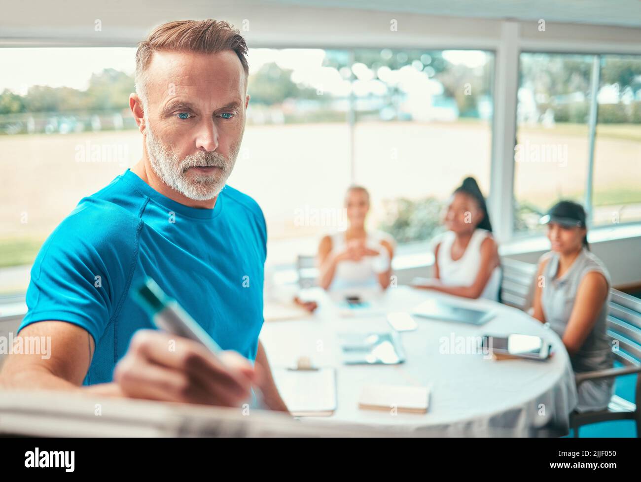 This is the spot where youll win against your opponent. a handsome mature coach standing and writing a game plan while his tennis team listen. Stock Photo
